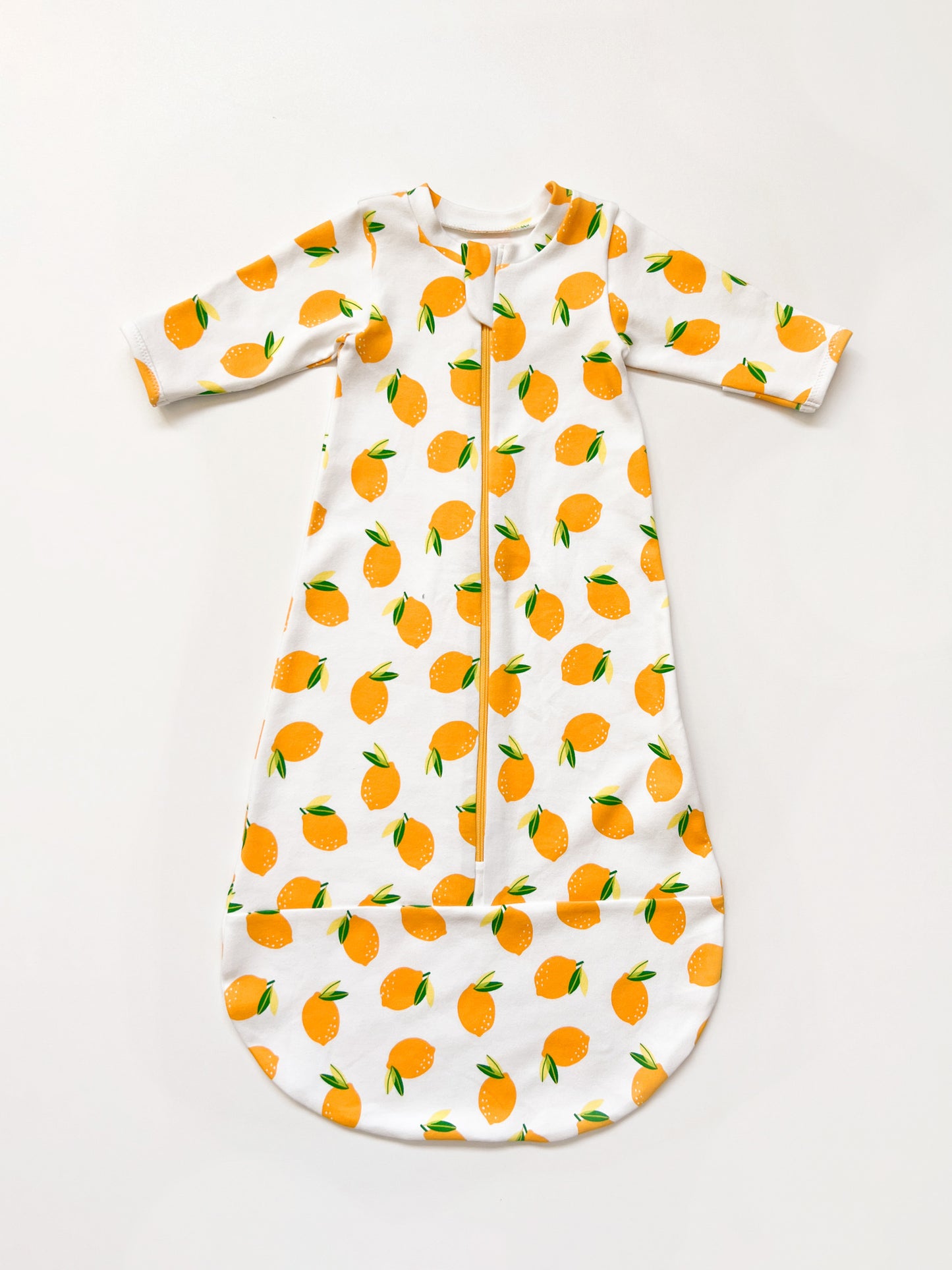 Flatlay of a baby sleepsack with zipper. The sleepsack is made in a white knit fabric with lemon print.