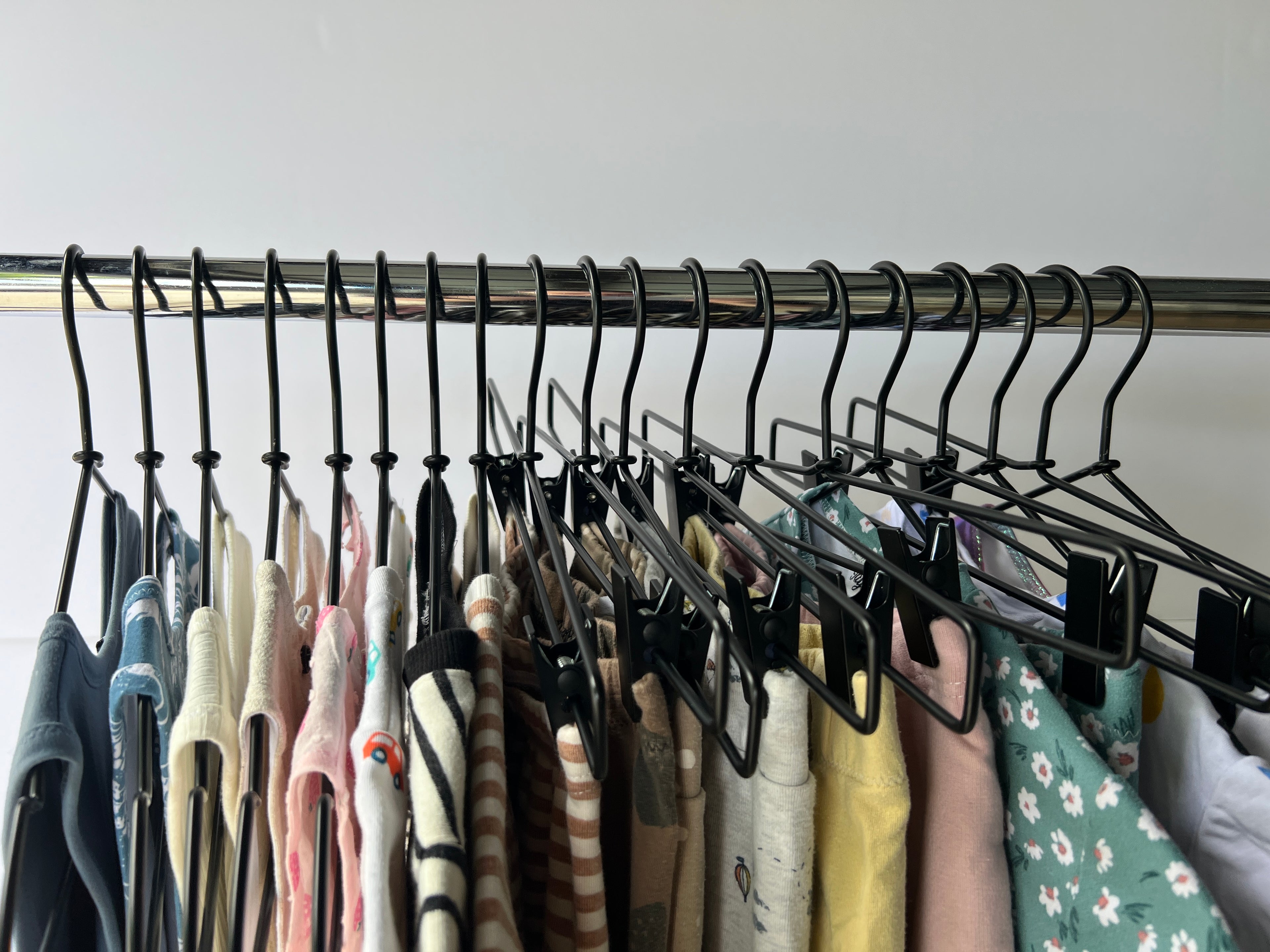 On a silver rack hangs 19 hangers of sewn kids clothing items: tank tops, dresses, t-shirts, long sleeve sweaters, shorts, leggings, joggers, and swimwear.